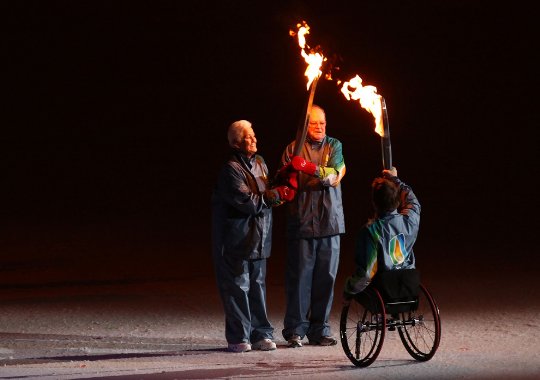 Fotografía de un hombre en silla de ruedas cambiando la antorcha con otras dos personas