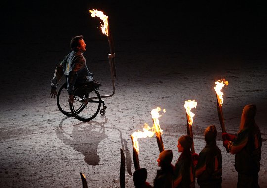 Fotografía un hombre en silla de ruedas portando la antorcha olímpica 