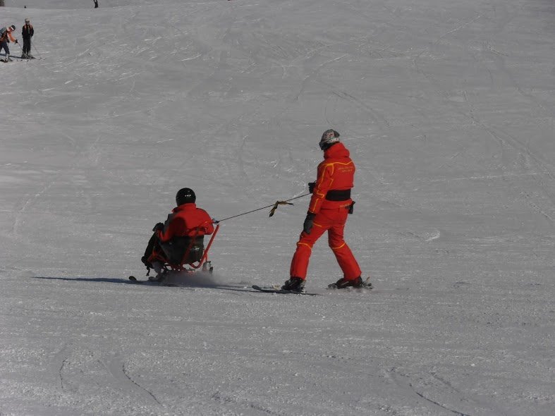 Fotografía de monitor de esquí bajandpo con discapacitado en silla