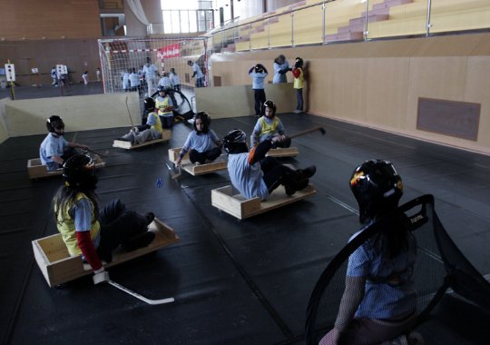 Fotografía de grupo de niños en cajones simulando sillas de ruedas jugando el hockey