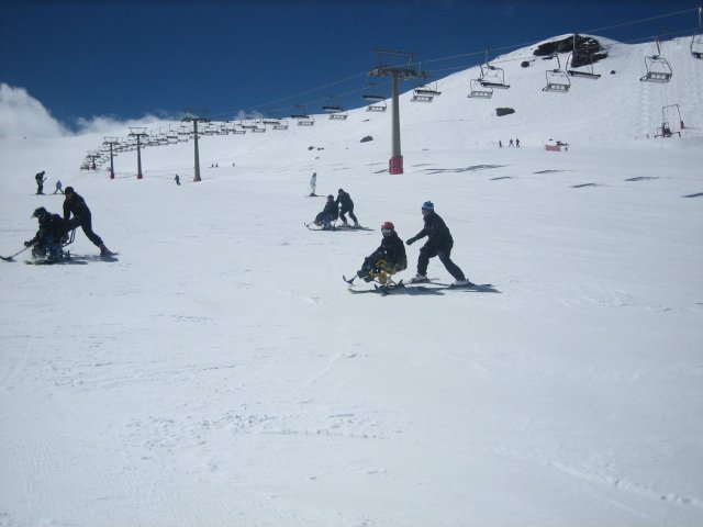 Fotografía de grupo de esquiadores adaptados bajando por pistas con sus monitores