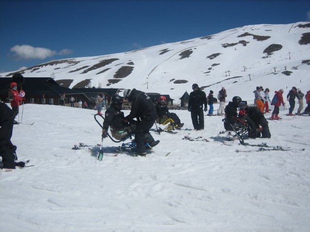 Fotografía de esquiadores preparándose en las sillas ayudados por sus monitores