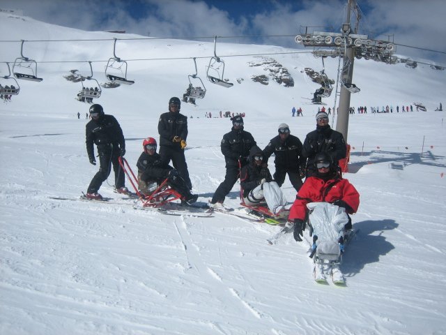 Fotografía de grupo de esquiadores adaptados con sus monitores bajando pistas